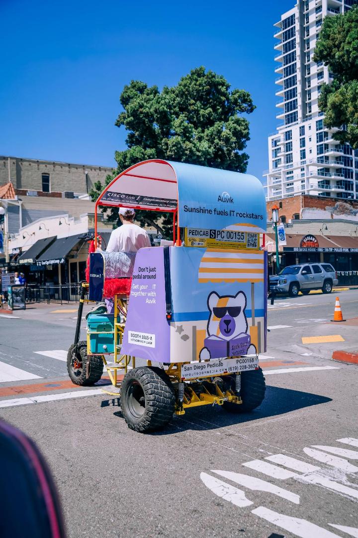 Rear of an Auvik-wrapped chariot with a cartoon bear and Cisco Live complimentary rides banner crossing a Gaslamp street