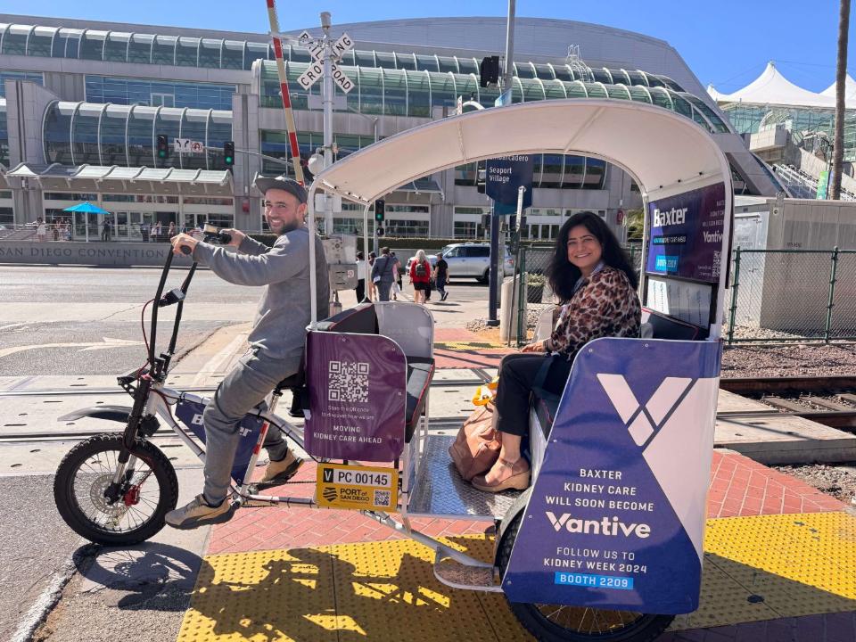 A smiling rider in a Baxter and Vantive wrapped pedicab at the Convention Center crossing