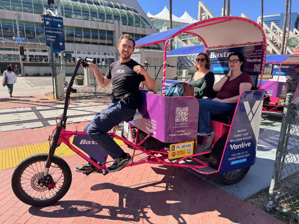 Driver and two riders in a pink pedicab wrapped for Baxter and Vantive outside the San Diego Convention Center