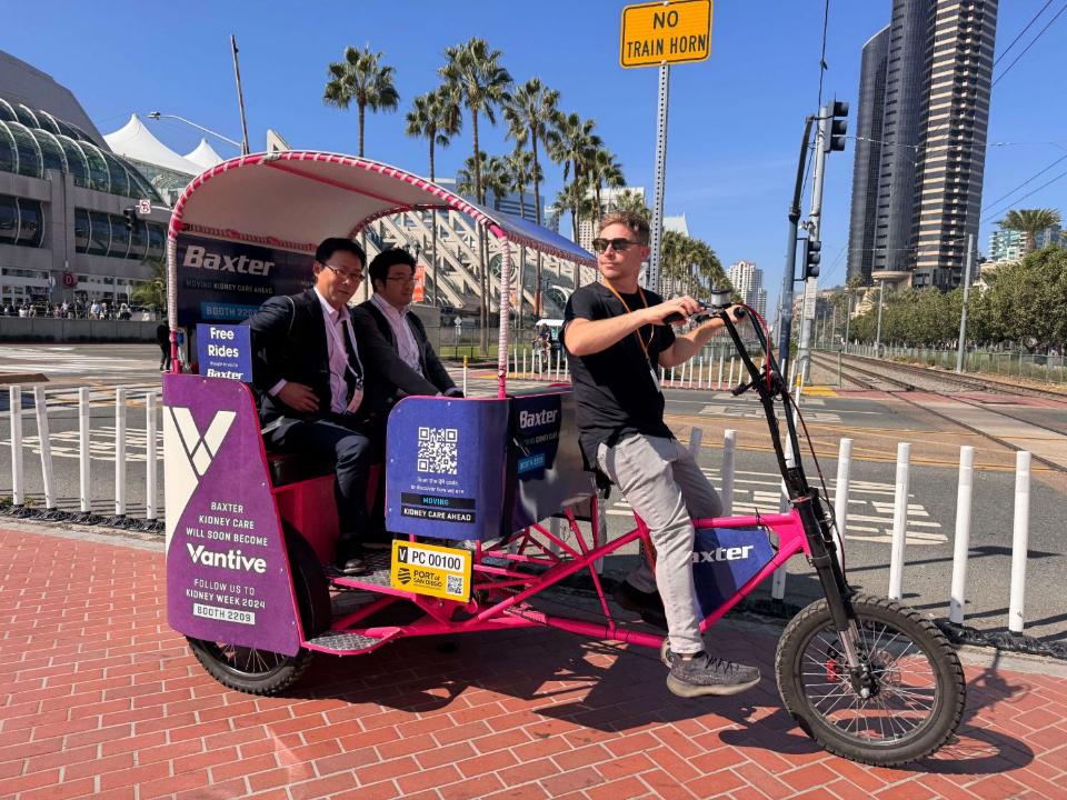 Two attendees in a wrapped pedicab with a Free Rides sign brought to them by the sponsor