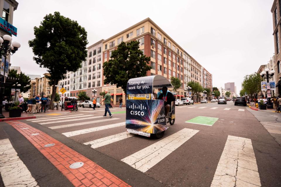 A Cisco wrapped pedicab reading Making AI work for you crossing a Gaslamp intersection