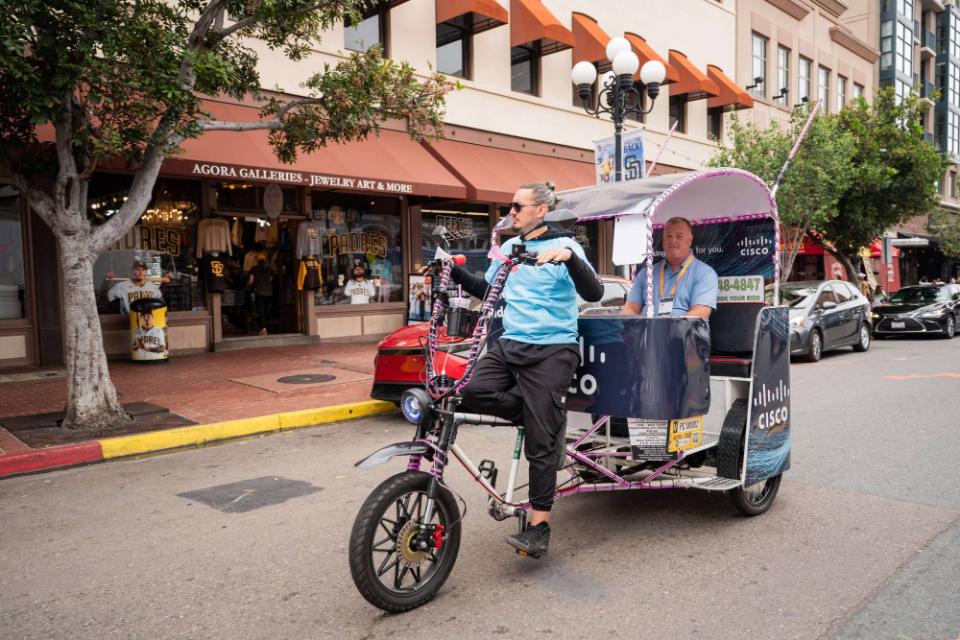 A driver carrying a conference attendee in a Cisco wrapped pedicab past a Padres store