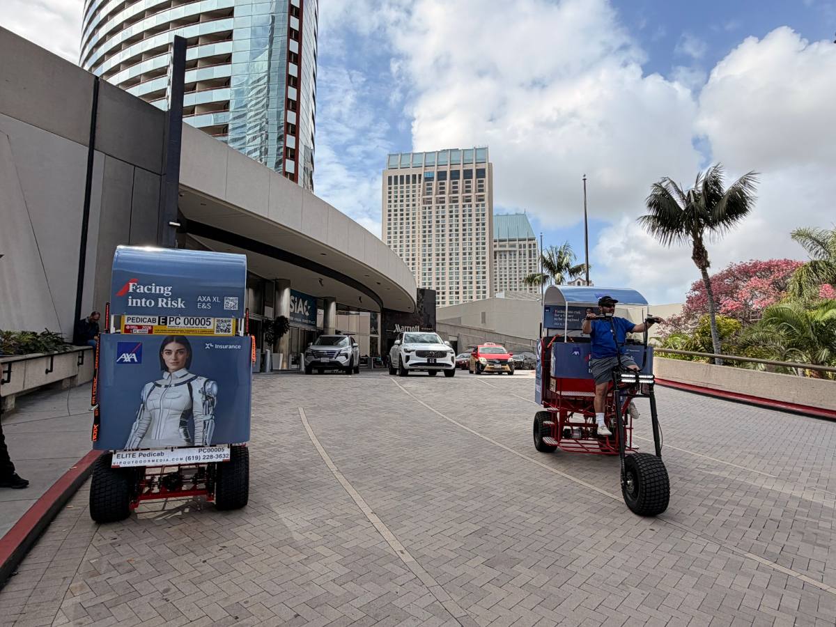 Two wrapped electric pedicabs and a driver at the Marriott Marquis entrance next to the San Diego Convention Center