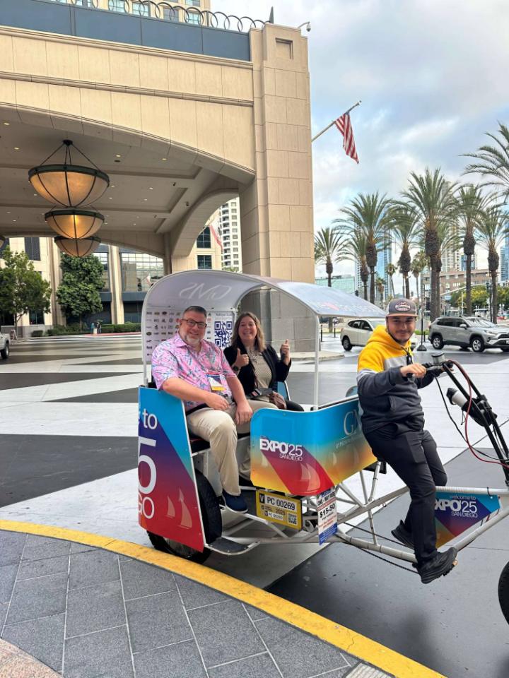 Two expo attendees giving a thumbs up from a wrapped pedicab outside a downtown hotel