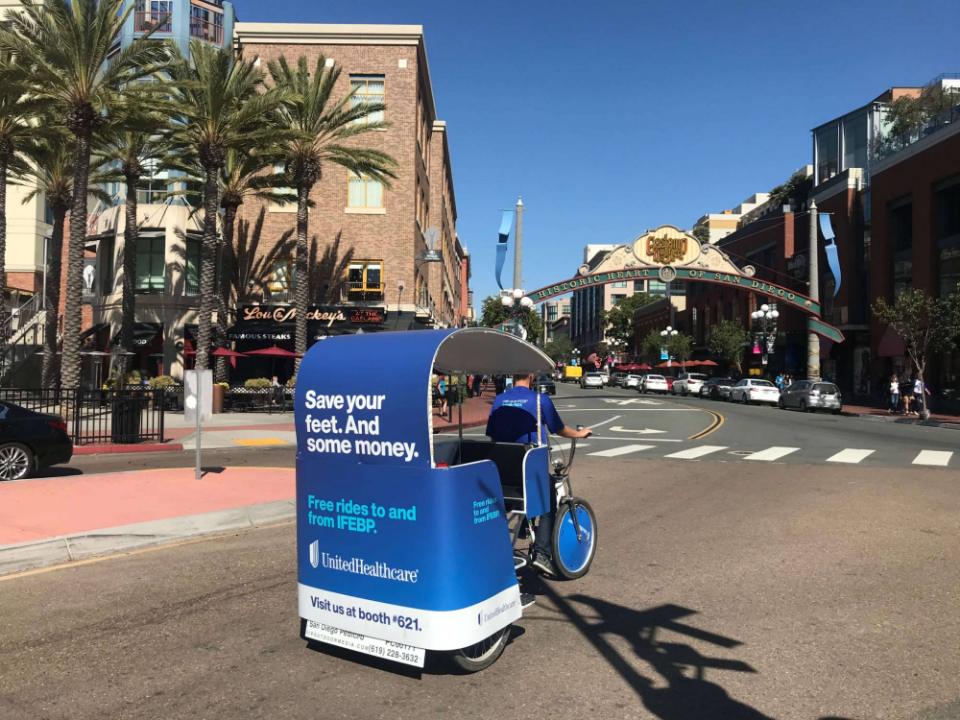A UnitedHealthcare wrapped pedicab reading Save your feet and some money, under the Gaslamp Quarter arch