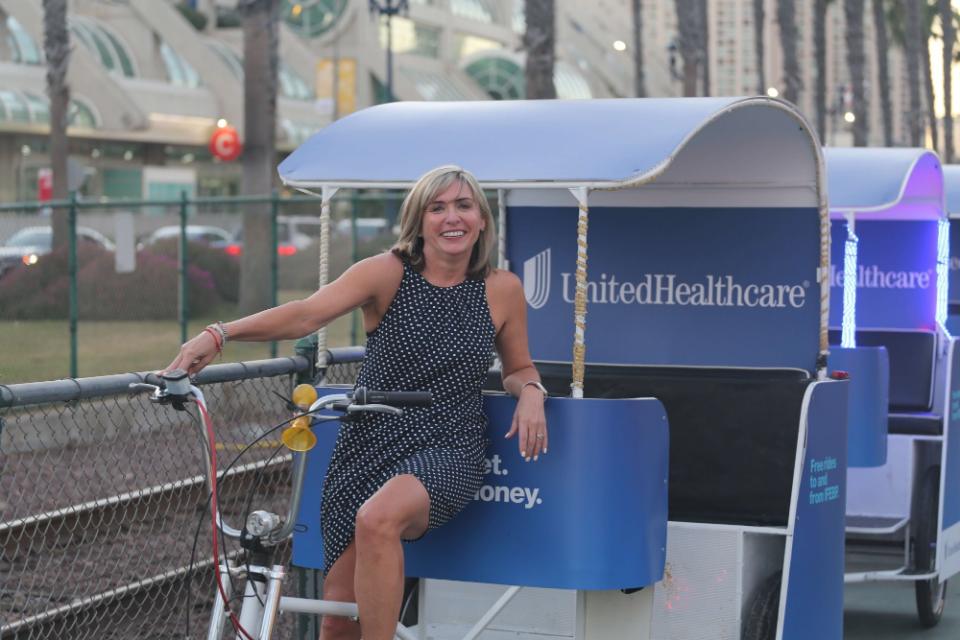 A smiling woman posing on a UnitedHealthcare wrapped pedicab by the Convention Center