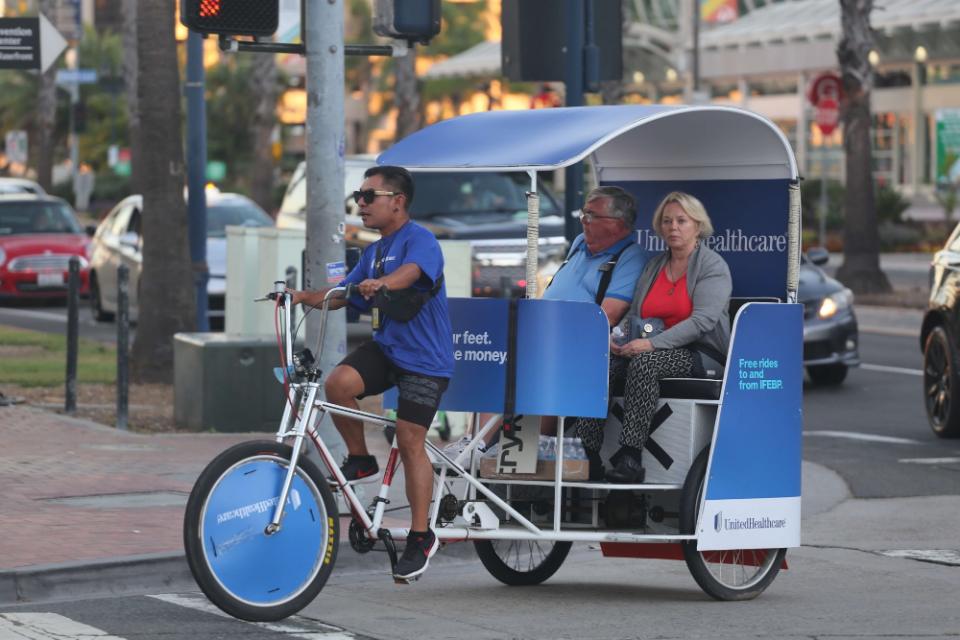 Driver carrying two riders in a UnitedHealthcare wrapped pedicab near the Convention Center
