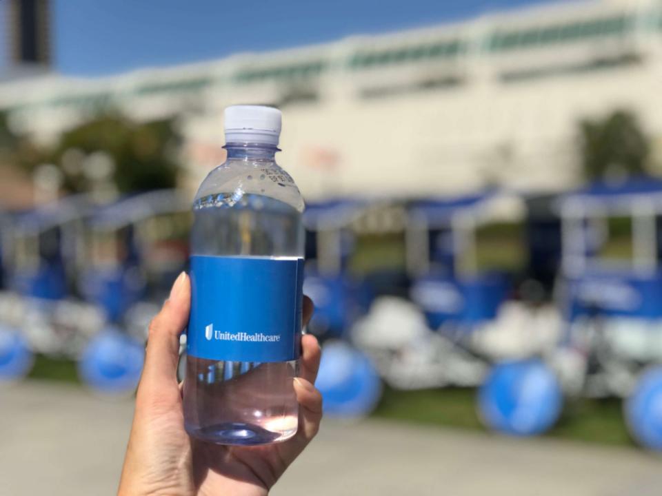 A UnitedHealthcare branded water bottle held up in front of the wrapped pedicab fleet